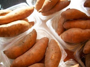 Several clear plastic containers filled with whole sweet potatoes are displayed on a surface, ready to be used in your next Seattle prepared meal delivery.