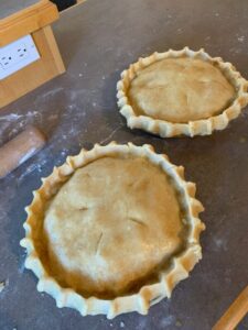 Two unbaked pies with crimped edges and slits on top are placed on a floured countertop, ready for Chef Ruben's holiday baking session. A rolling pin and an electrical outlet are partially visible in the background.