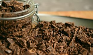 A glass jar filled with chocolate chunks lies on its side, spilling onto a wooden surface covered with more chocolate chunks—a perfect setting for holiday baking.