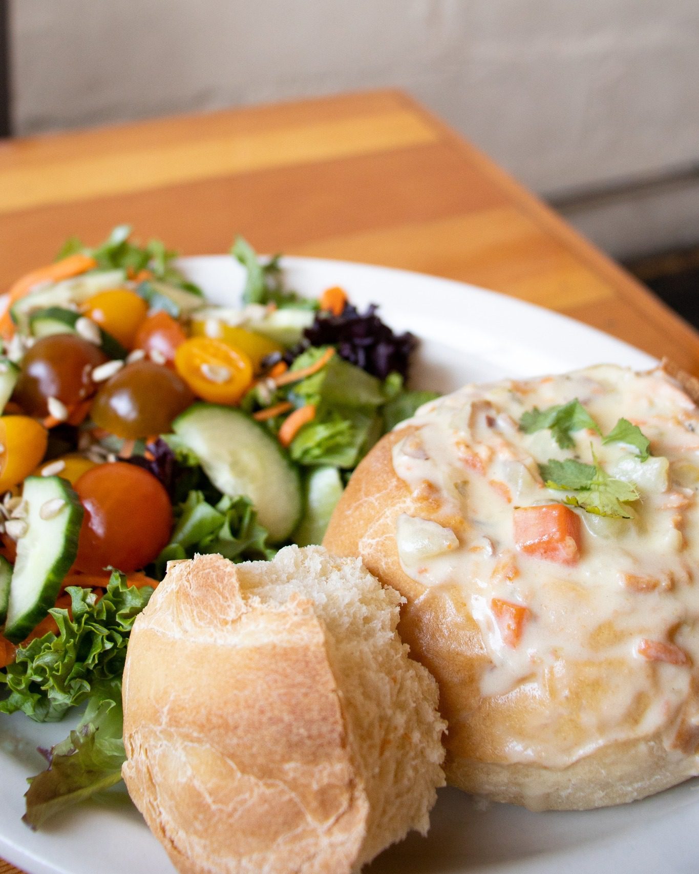 A plate on a table with a garden salad and clam chowder in a bread bowl