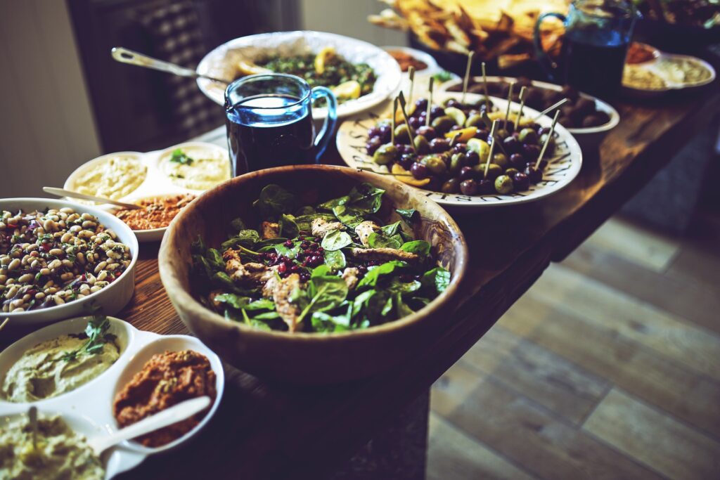 A table is set with various dishes, including a large bowl of salad rich in antioxidants, skewered olives, small bowls of dips, and plates of assorted vegetables and snacks.