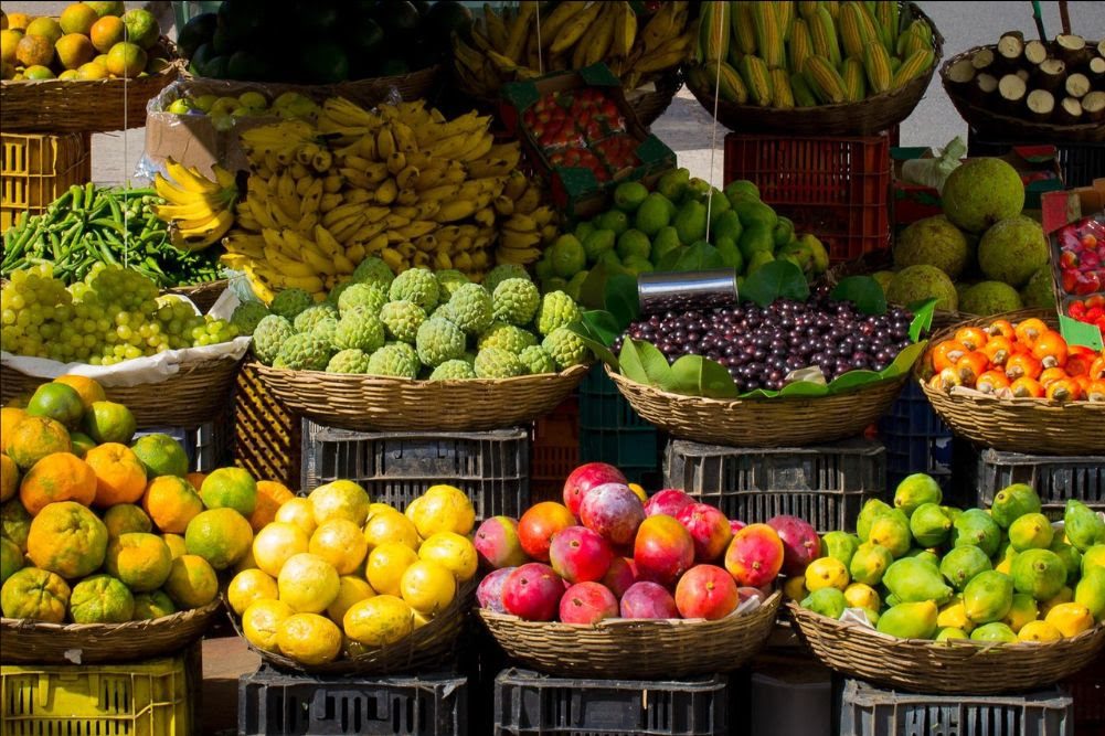 Various fruits, including bananas, lemons, mangoes, pomegranates, and grapes, displayed in baskets at an outdoor market near Bellingham restaurants.