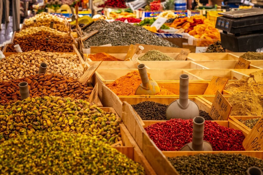 Market stall featuring wooden crates filled with various spices, herbs, nuts, and dried fruits in vibrant colors, organized with scoops and price tags. Discover fall spices from around the world that go beyond pumpkin spice to elevate your seasonal dishes.