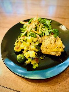 A plate with herb-roasted chicken, sautéed Brussels sprouts with diced potatoes, and a side salad prepared by Chef Jane Hall.