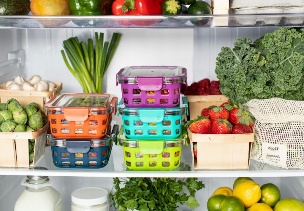 A refrigerator shelf filled with winter fresh fruits, vegetables, and four colorful, reusable food containers to spruce up your kitchen.