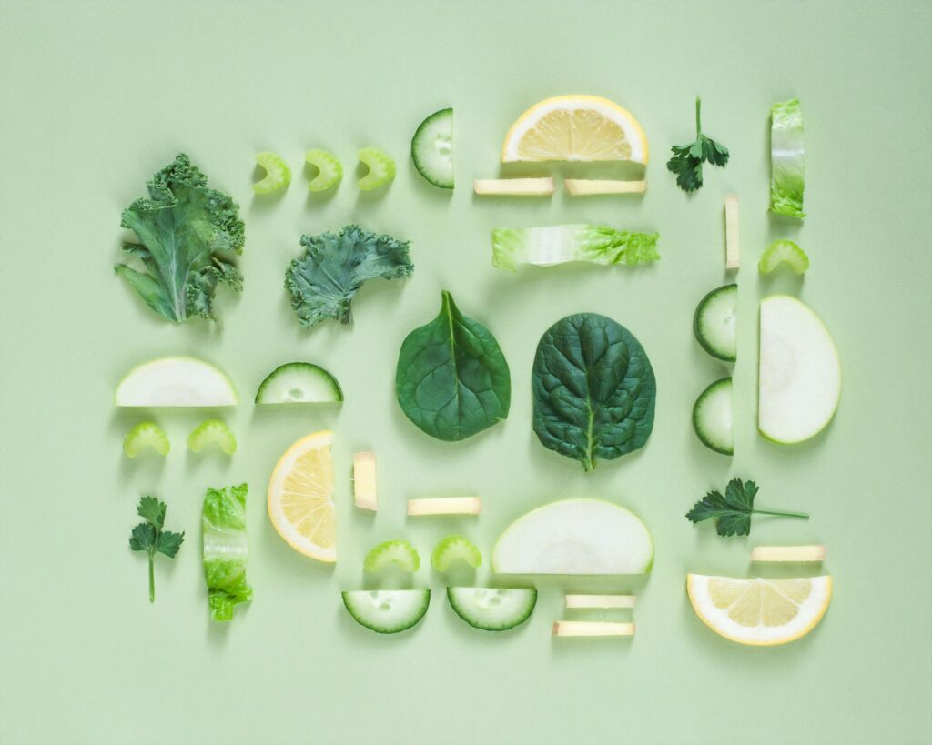 A flat lay of assorted green vegetables and lemon slices, perfect for a spring greening theme, arranged symmetrically on a light green background.