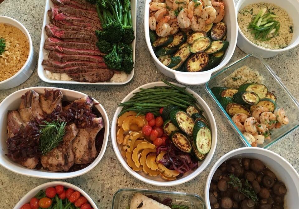 A variety of dishes on a table, including sliced beef, shrimp, sautéed vegetables, grain dishes, green beans, and a bowl of mushrooms.