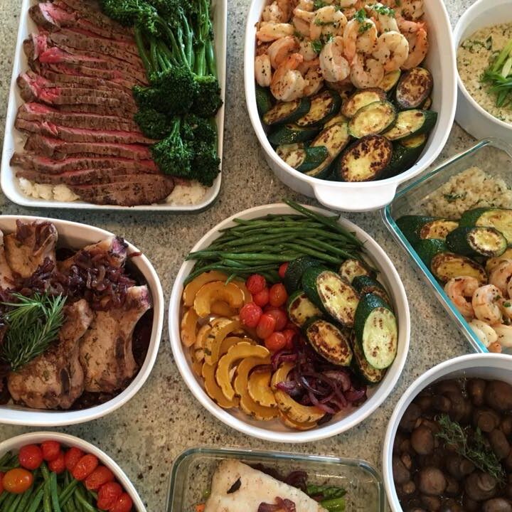 A variety of dishes on a table, including sliced beef, shrimp, sautéed vegetables, grain dishes, green beans, and a bowl of mushrooms.