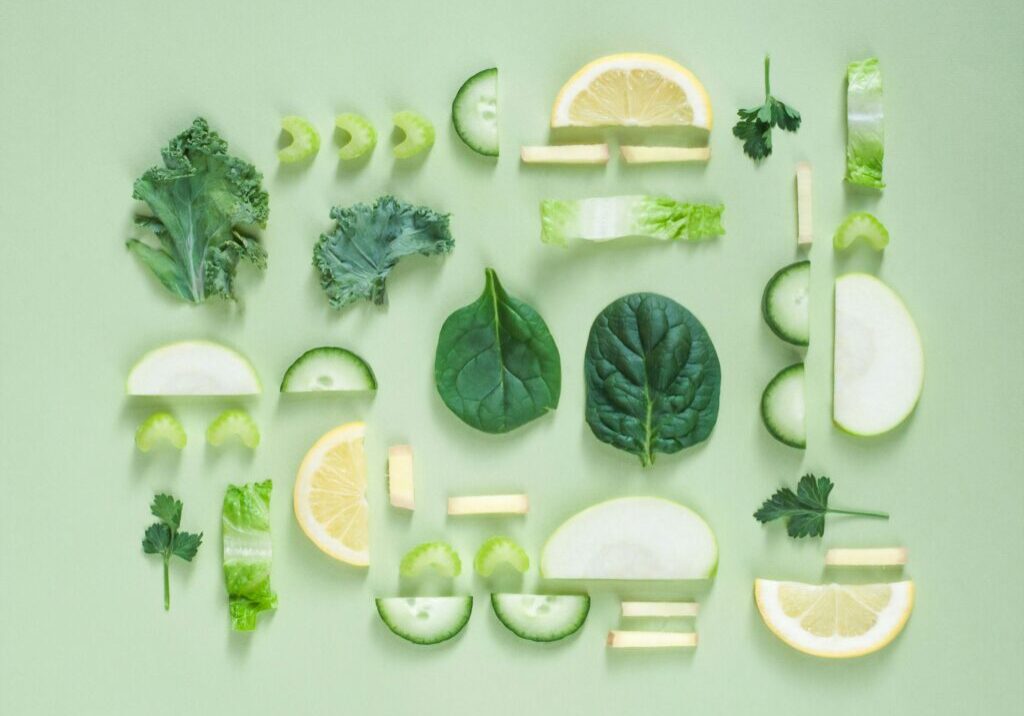 A flat lay of assorted green vegetables and lemon slices, perfect for a spring greening theme, arranged symmetrically on a light green background.