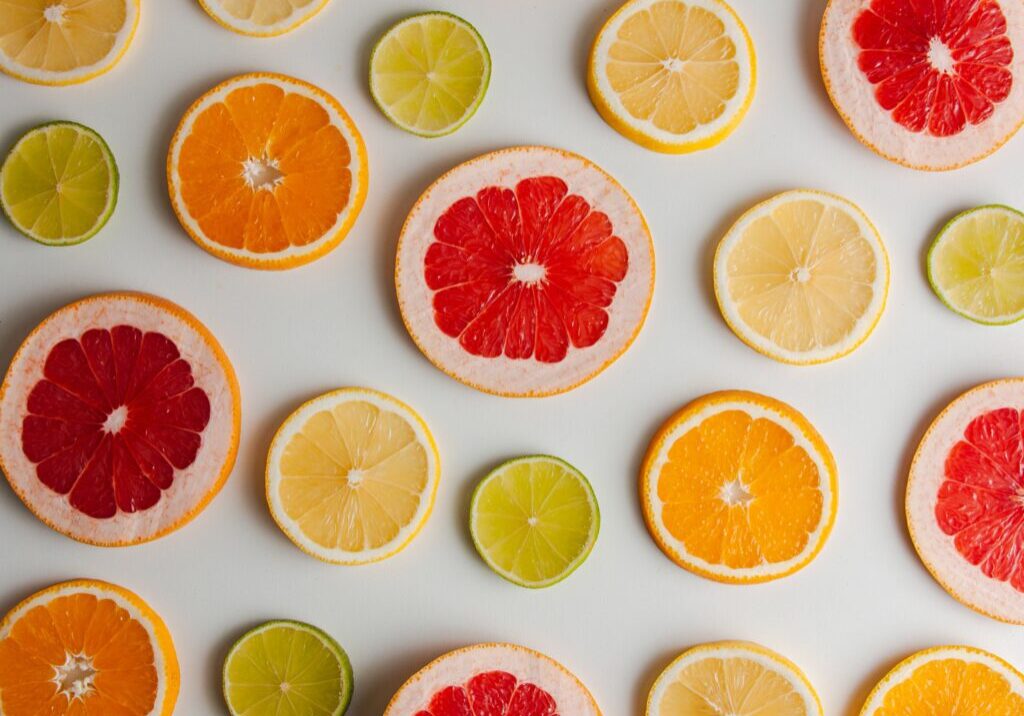 Slices of citrus fruits, including grapefruit, orange, lemon, and lime, arranged in a scattered pattern on a white surface. These vibrant colors of citrus in winter create a refreshing and visually appealing display.
