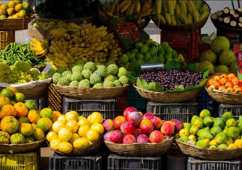 Various fruits, including bananas, lemons, mangoes, pomegranates, and grapes, displayed in baskets at an outdoor market near Bellingham restaurants.