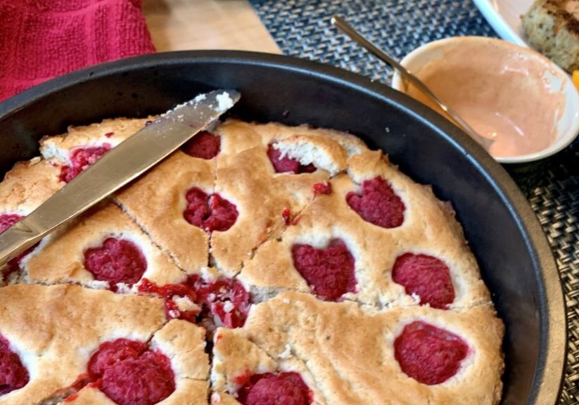 white vegan pastry studded with red saspberries in a round black pan